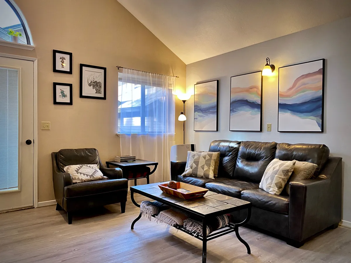 A cozy, well-lit living room with a comfortable leather sofa facing a coffee table and art-adorned wall, evoking evenings spent relaxing as a family—possibly for movie streaming sessions or intimate conversations after exploring nearby attractions.
