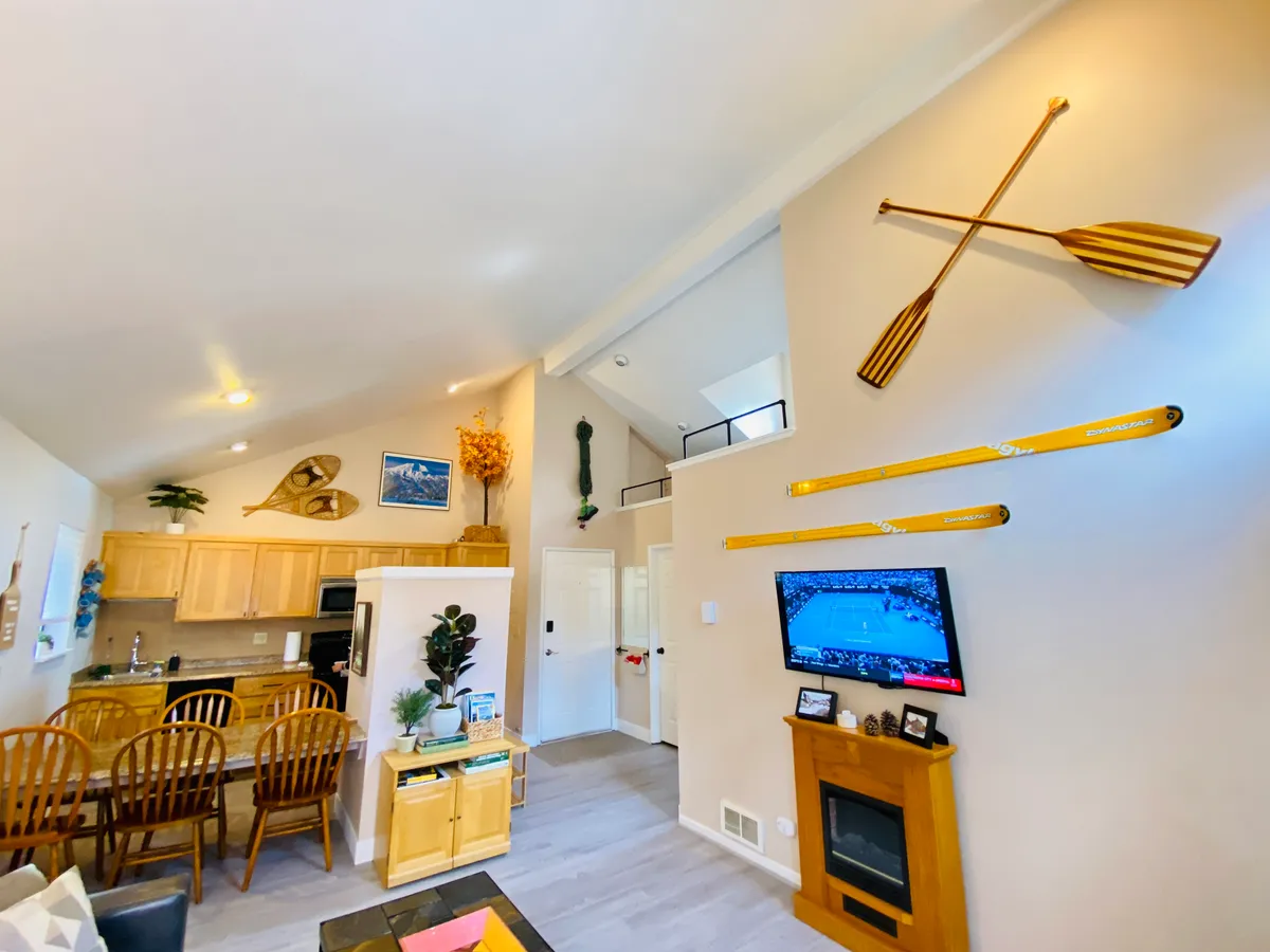 A freshly renovated condo interior featuring a warm fireplace, stylish kitchen, inviting dining table, and playful decorative oars, all set in a bright, cozy open-plan living space.