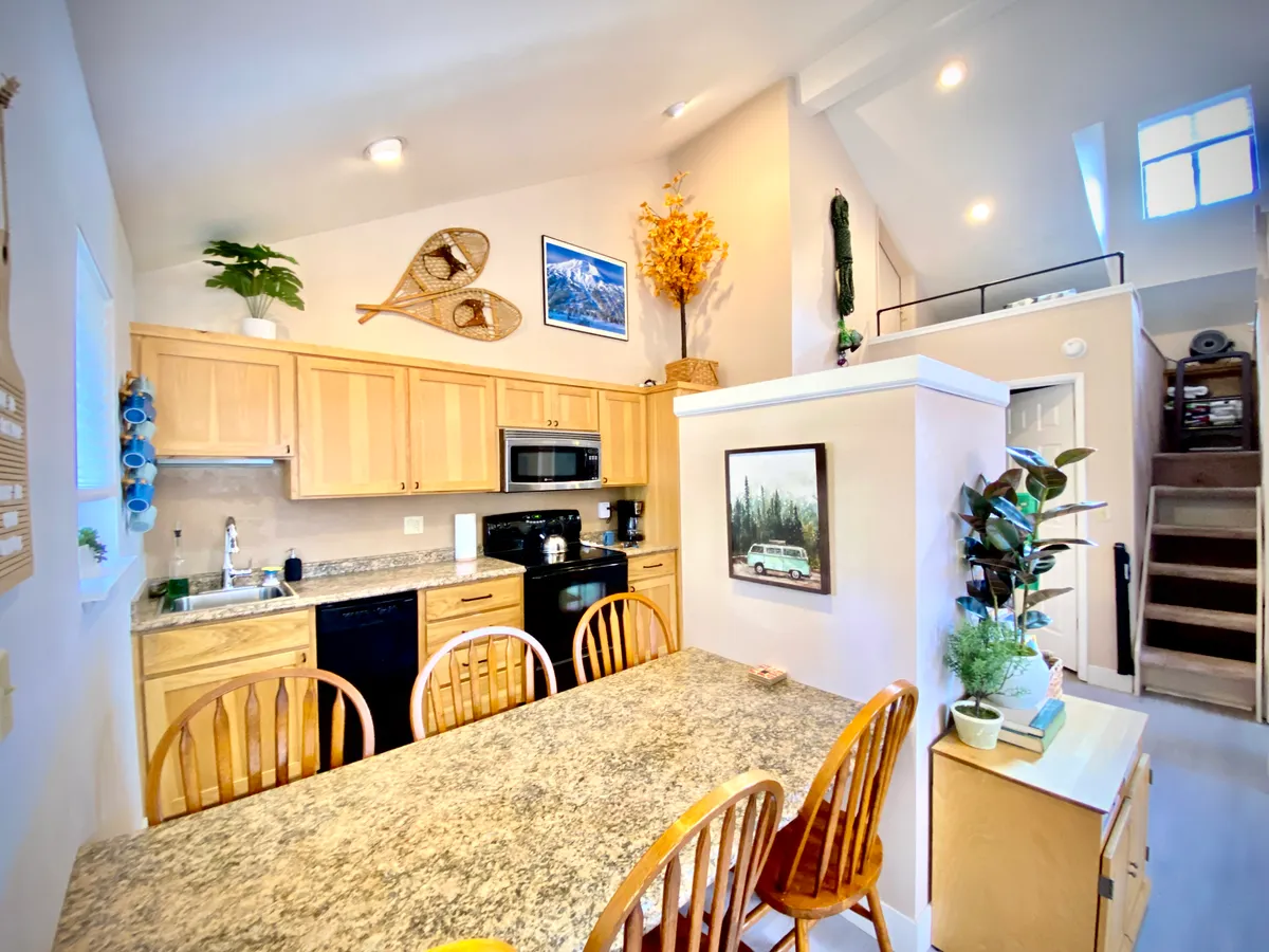 A welcoming kitchen and dining area with a granite countertop, stylish wooden chairs, and decorative wall art. The space is bathed in morning light, creating an ideal setting for cooking, breakfast, or evening celebrations.