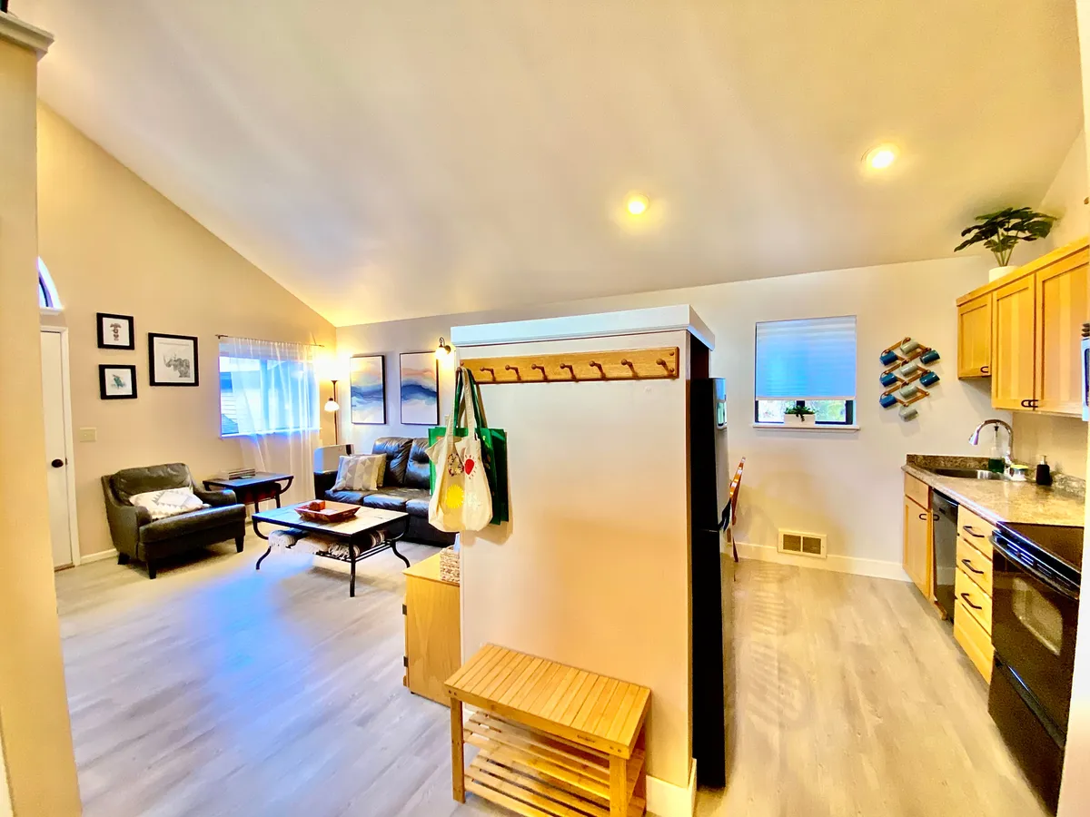 This inviting interior image presents the main living area, featuring comfortable seating, a kitchen counter, decorative wall art, and cabinetry. The open flow between living and kitchen spaces highlights modern comfort and hospitality, suggesting an easy transition from entry to relaxation after a day of adventure.